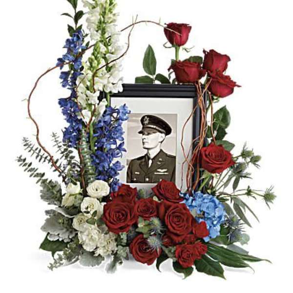Floral tribute around a framed military portrait with red roses and blue-white flowers