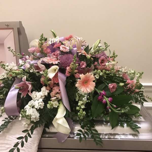 Large pastel floral arrangement with ribbons on a casket