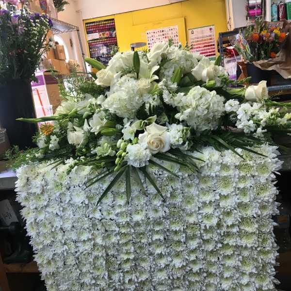 Large white floral arrangement with roses and lilies over a dense chrysanthemum base