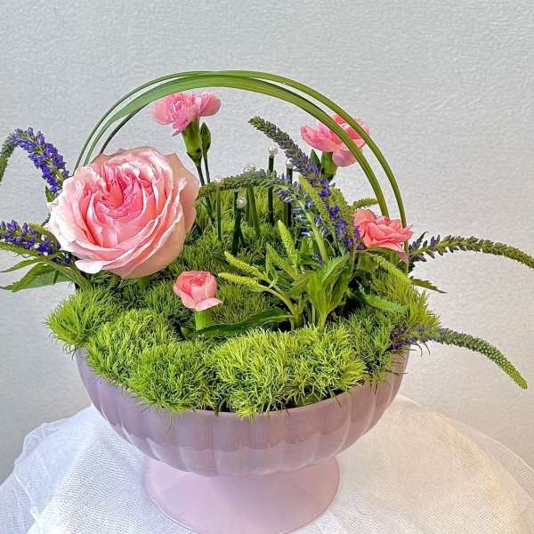 Pink roses and carnations arranged in a pink pedestal bowl