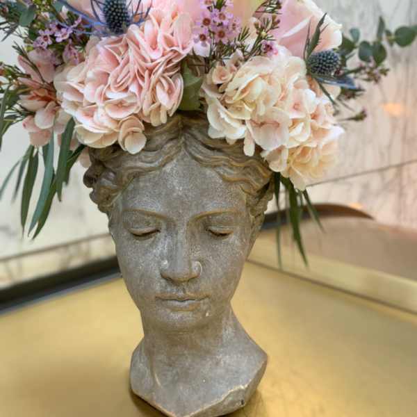 Floral arrangement in a stone bust vase with pale pink and cream blooms