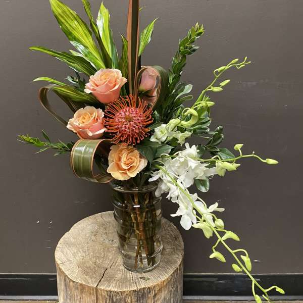 Tropical floral arrangement in a glass vase with peach roses and white orchids
