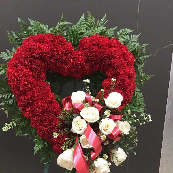 Heart-shaped red carnation wreath with white roses and pink ribbon