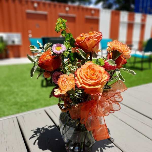 Orange rose bouquet in a glass vase with an orange ribbon