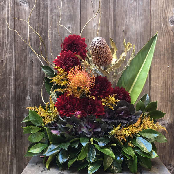 Arrangement of red and orange flowers with glossy leaves and tall branches