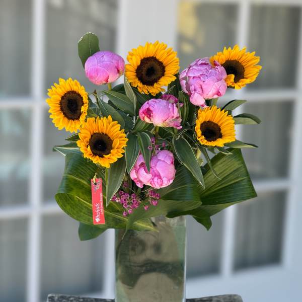 Sunflowers and pink peonies arranged in a tall glass vase