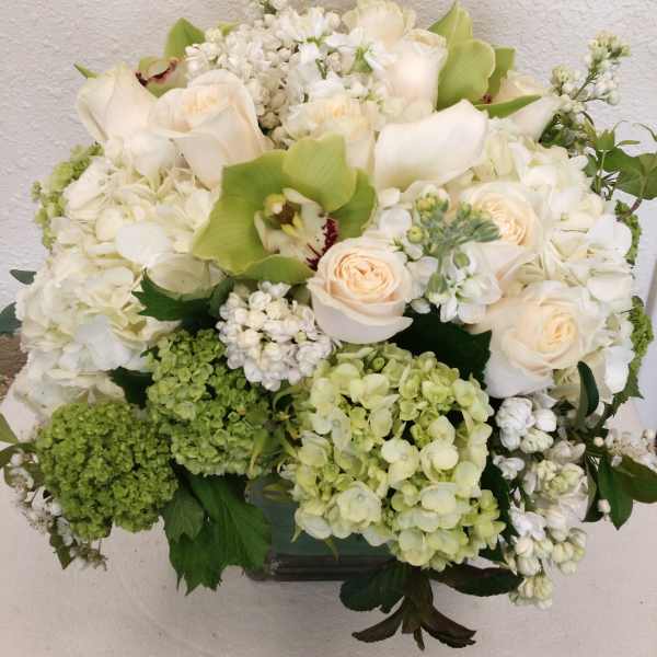 White and pale green floral arrangement with roses and orchids in a vase