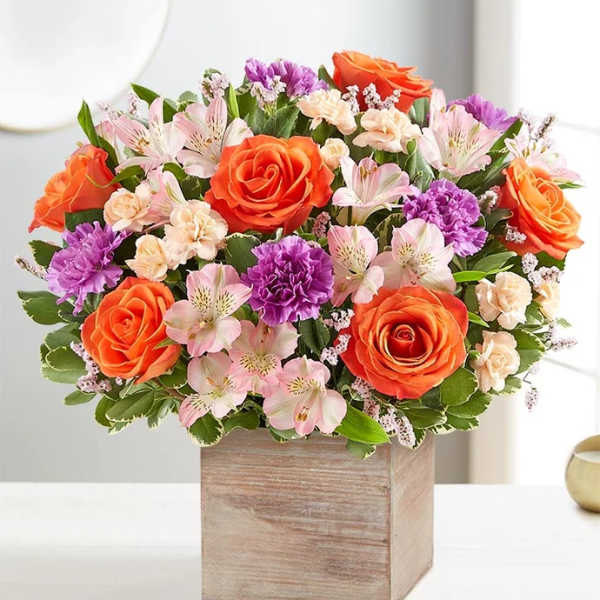 Mixed bouquet of orange roses, pink alstroemeria, and purple carnations in a wooden box