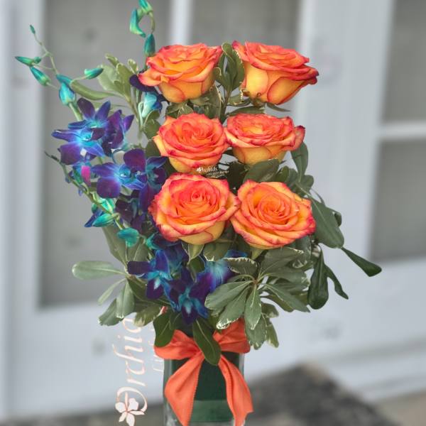 Orange roses with blue orchids in a glass vase