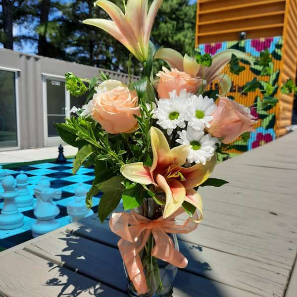 Peach roses and lilies in a glass vase with a ribbon
