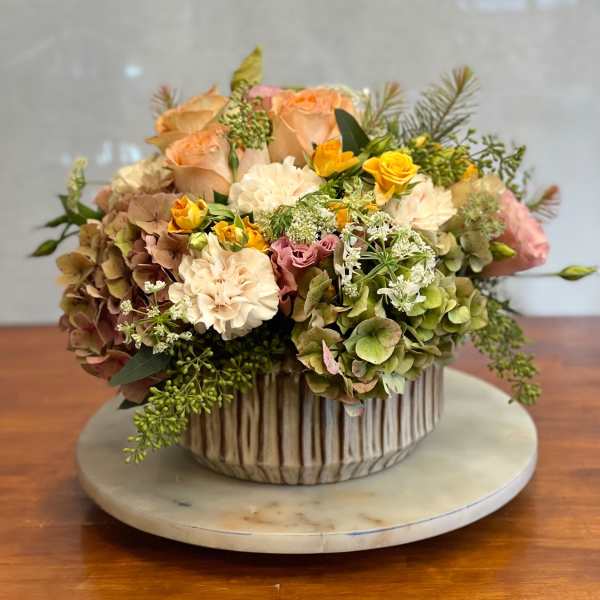 Mixed floral arrangement in a ribbed ceramic vase with peach, cream, and yellow blooms