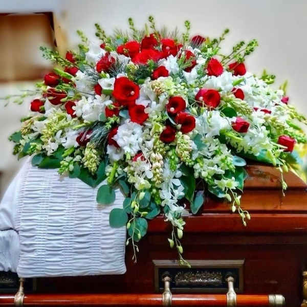 Red and white casket spray of roses and mixed white flowers on a wooden casket