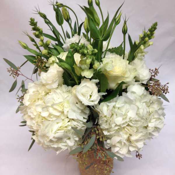 White hydrangeas and roses in a woven basket with tall green buds