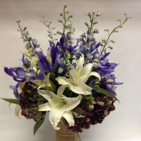 Bouquet of white lilies and purple irises in a burlap-wrapped vase