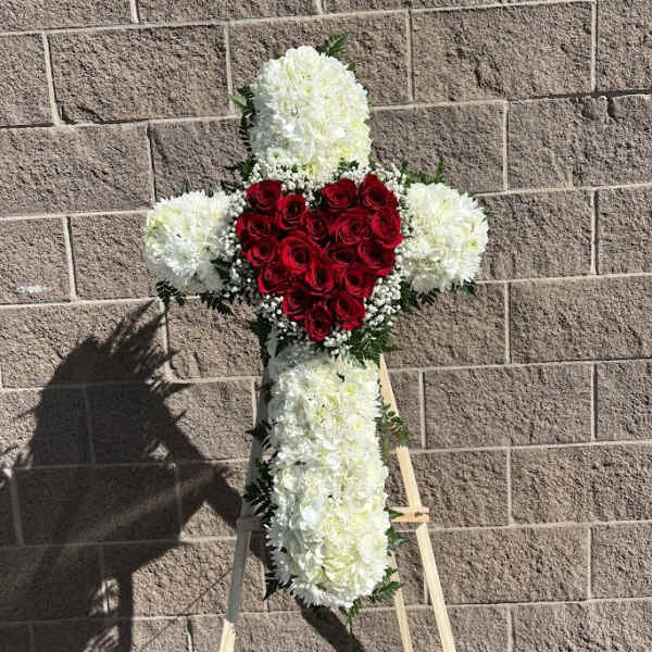 Cross-shaped floral tribute with red roses and white flowers on an easel