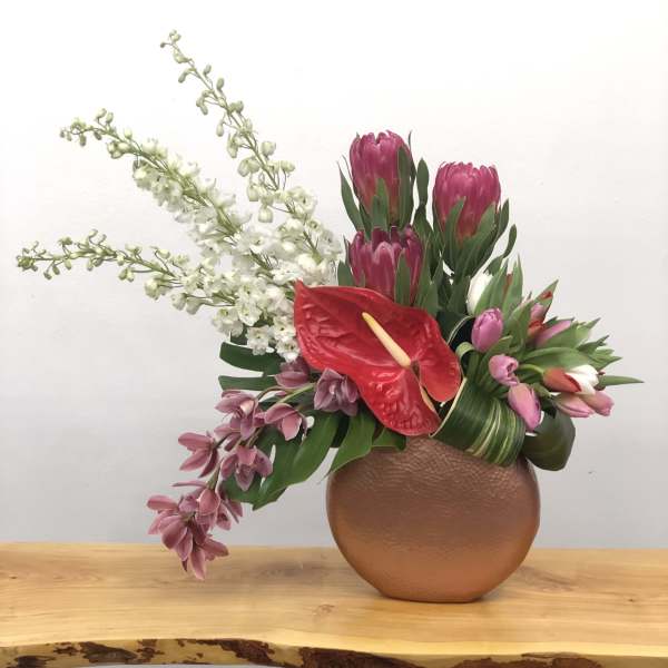 Pink protea and orchids arranged in a round copper vase