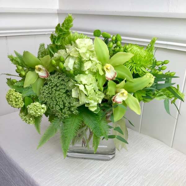 Green floral arrangement in a glass vase with orchids and hydrangeas