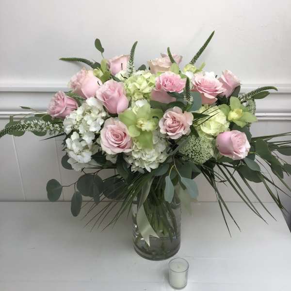 Large arrangement of pink roses, green orchids, and white hydrangeas in a clear glass vase with a small votive candle.