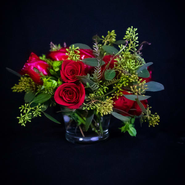 Red roses arranged in a clear glass vase with greenery