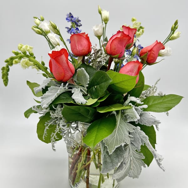 Red roses and white flowers arranged in a clear glass vase.