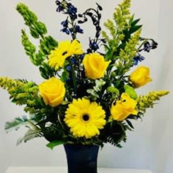 Yellow gerbera daisies and roses in a dark vase