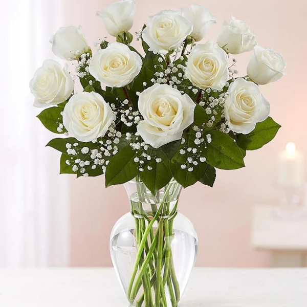 Arrangement of white roses with small white filler flowers in a clear glass vase.