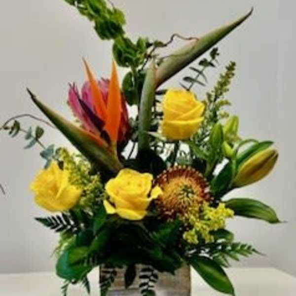 Tropical floral arrangement with yellow roses in a square vase
