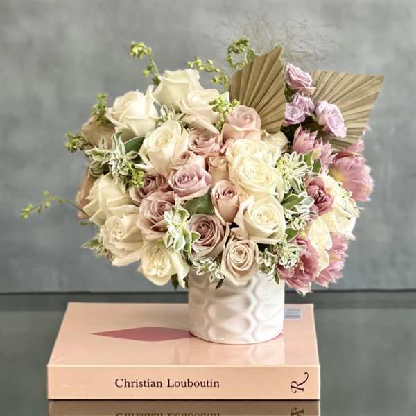 Pastel pink and cream rose arrangement with ruffled blooms in a white vase set on fashion books