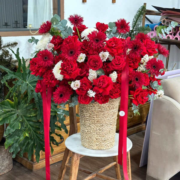 Large red floral arrangement in a woven basket with ribbon streamers