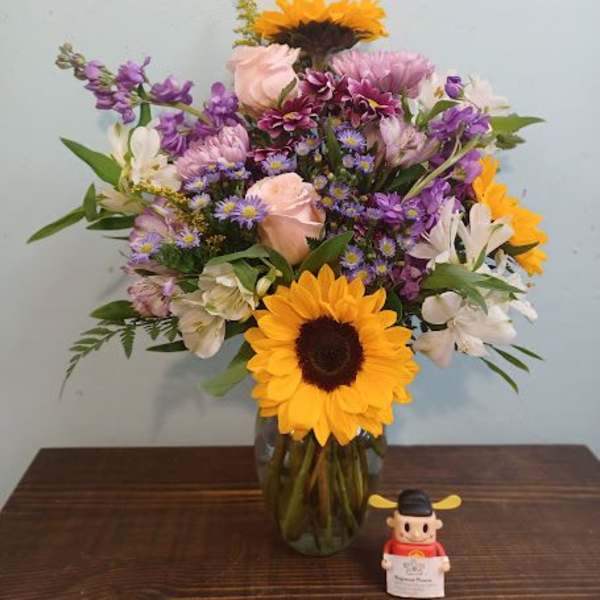 Mixed bouquet in a glass vase with sunflowers, roses, and purple blooms