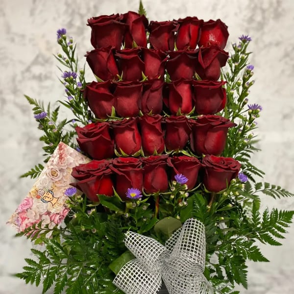 Tall arrangement of tiered red roses with small purple asters in a metal container with a silver bow