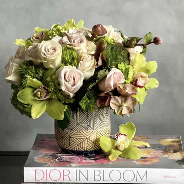Compact arrangement of blush roses and green orchids in a patterned vase on books