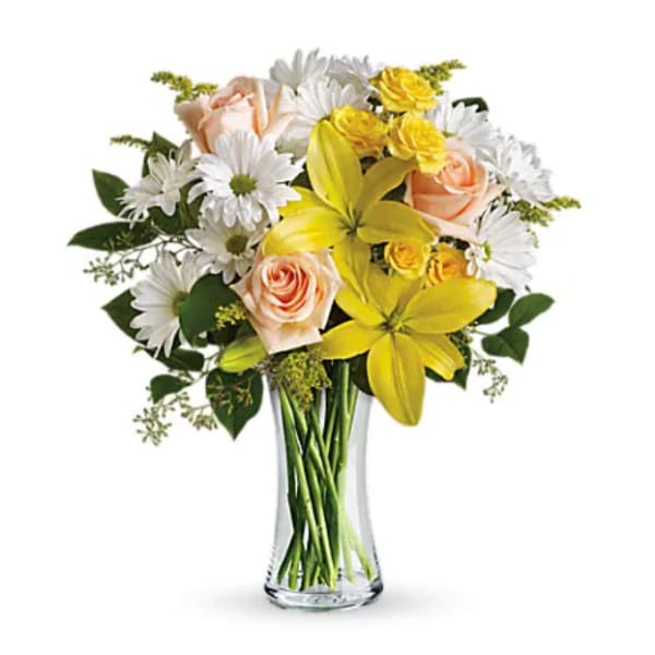 Bouquet of yellow lilies, peach roses, and white daisies in a clear glass vase