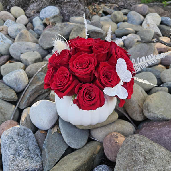 Red roses arranged in a white pumpkin-shaped vase with white butterfly accents