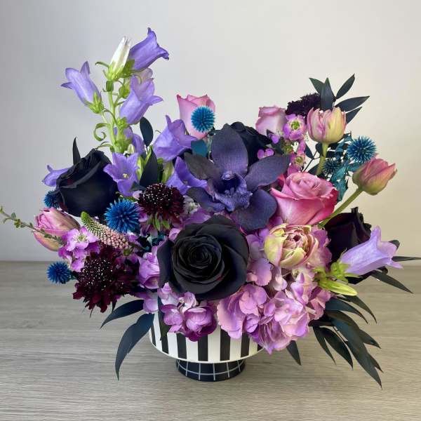 Purple and black floral arrangement in a striped vase