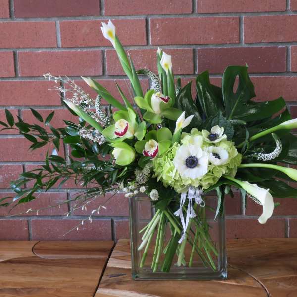 White calla lilies and green orchids in a glass vase