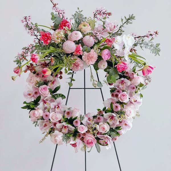 Pink floral wreath on a black stand with roses and orchids