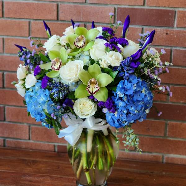 Bouquet of white roses, blue hydrangeas, and green orchids in a glass vase