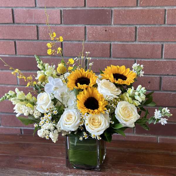 Sunflowers and white roses arranged in a square glass vase
