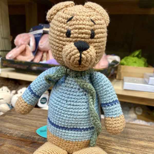 Crocheted teddy bear plush in a blue sweater sitting on a wooden surface