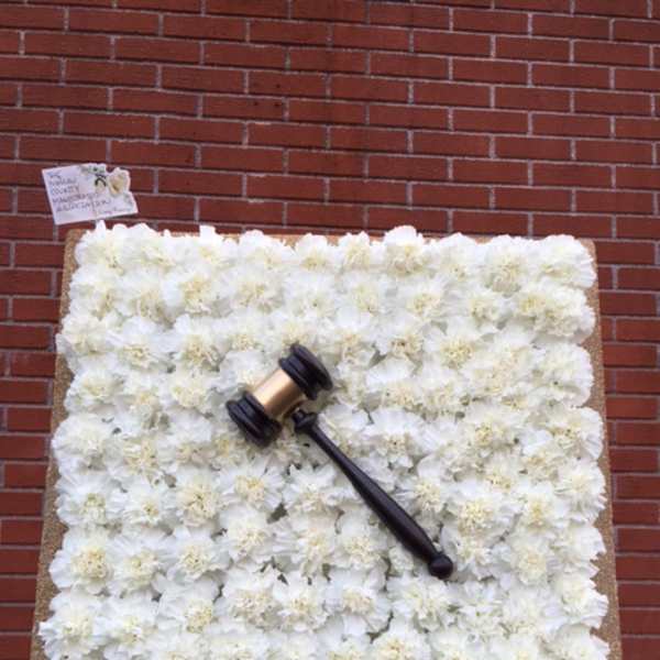 White floral memorial display with a gavel on an easel