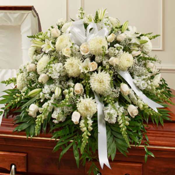 White funeral spray with lilies, roses, and ribbons on a casket