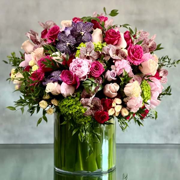 Large arrangement of pink roses, peonies, orchids, and green hydrangeas in a clear glass cylinder vase