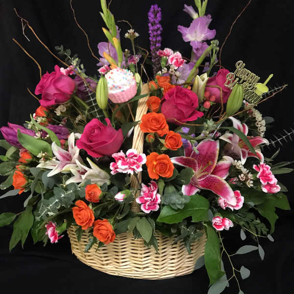 Basket arrangement of pink roses, orange roses, lilies, and a birthday topper
