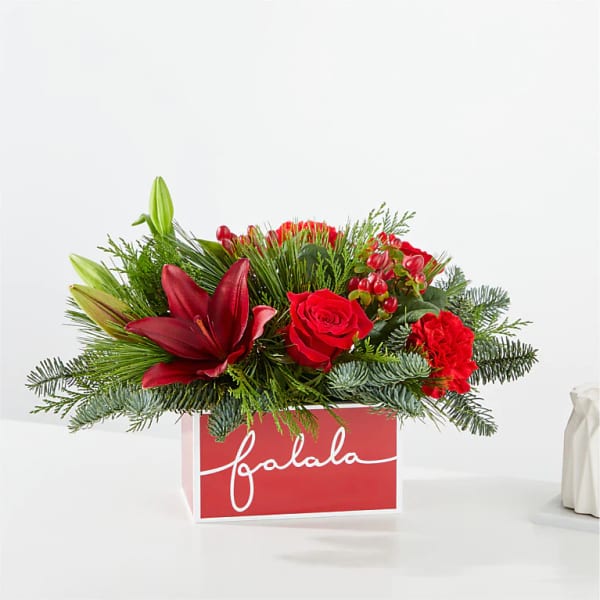 Red floral arrangement in a red gift box with evergreen accents