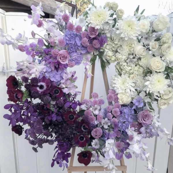 Large heart-shaped floral arrangement in purple, white, and burgundy tones on an easel
