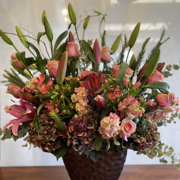 Pink lilies and roses arranged in a dark vase