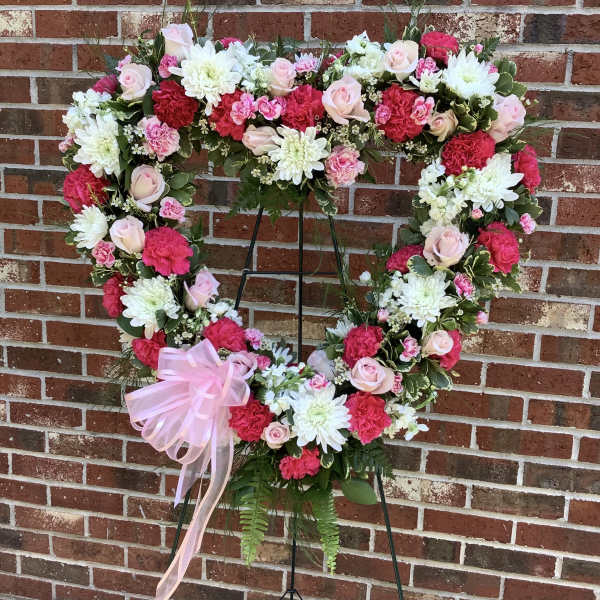 Heart-shaped floral wreath with pink and white flowers on a stand
