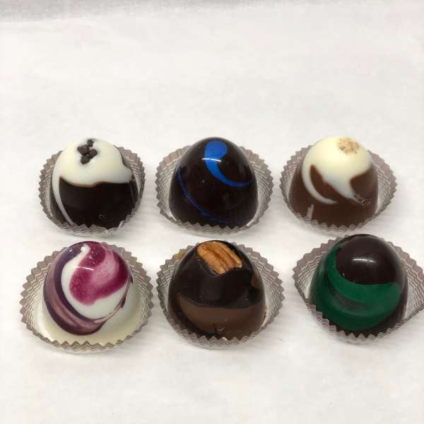 Set of six assorted round chocolate truffles in individual paper cups on a white surface