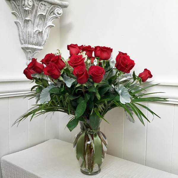Red roses arranged in a clear glass vase with greenery